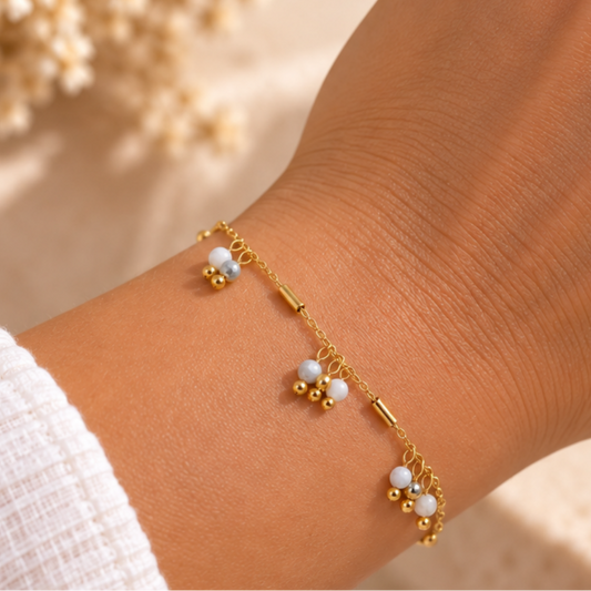 bracelet en acier inoxydable doré, orné de perles blanches et de pampilles. Un bijou délicat à porter seul ou avec d’autres bracelets