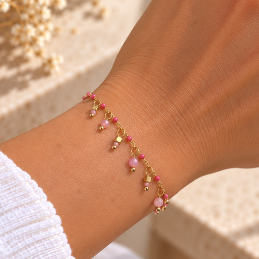bracelet en acier inoxydable doré, orné de perles roses et de pampilles. Un bijou délicat à porter seul ou avec d’autres bracelets